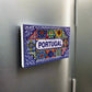 A decorative tile magnet featuring the word "PORTUGAL" in the center, surrounded by intricate floral and geometric patterns in bold colors, including red, blue, green, yellow, and white. This vibrant piece makes for a beautiful souvenir.