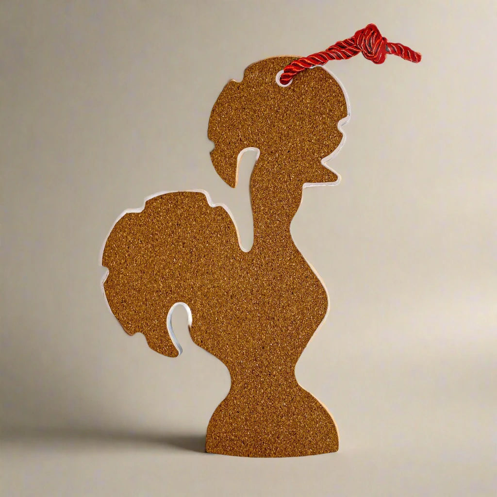 A rooster-shaped ornament made of brown cork material is standing upright against a plain background. The ornament, a charming souvenir from Portugal, has a red string looped through a hole at the top.