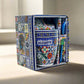 A colorfully patterned souvenir gift set from Algarve, Portugal, includes a ceramic mug with intricate designs and a blue spoon. The packaging is decorated with similar vibrant, multicolored patterns, showcasing a variety of geometric and floral motifs in a beautifully crafted box.