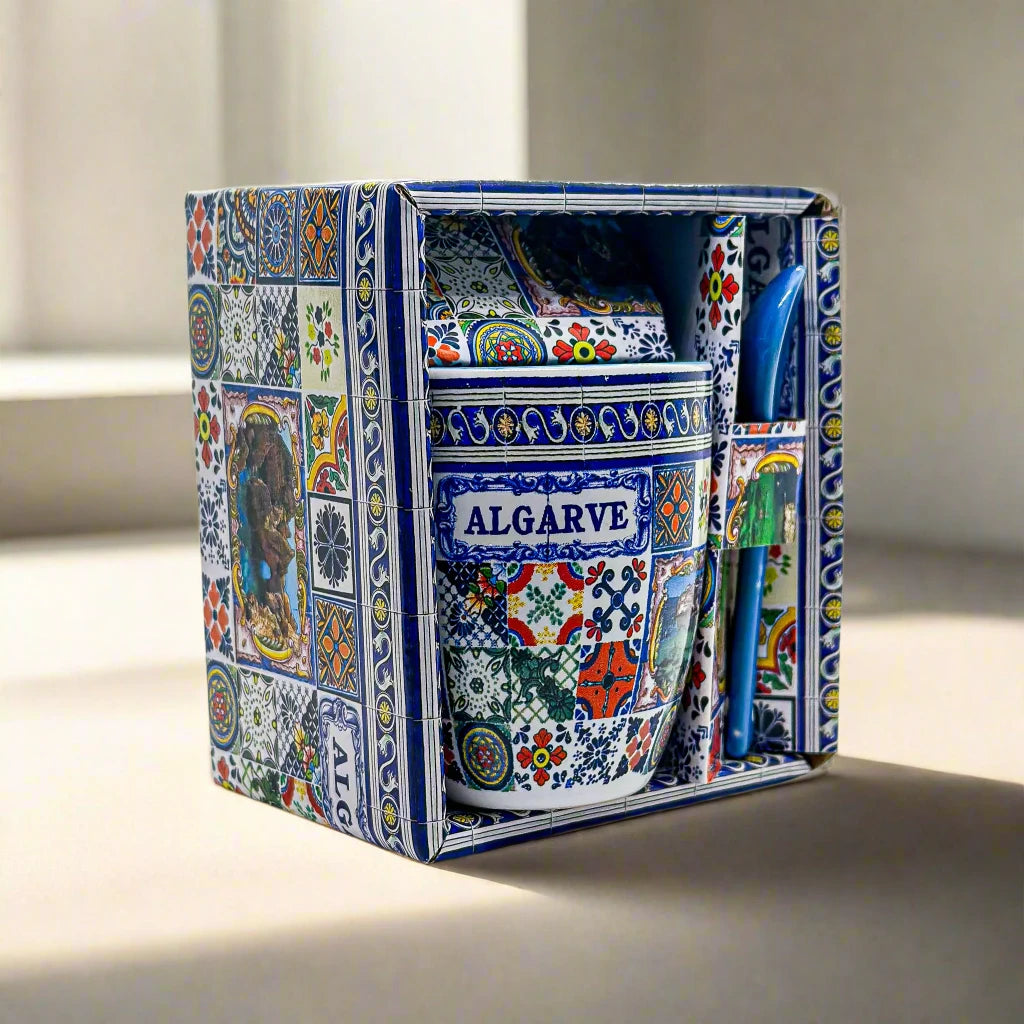A colorfully patterned souvenir gift set from Algarve, Portugal, includes a ceramic mug with intricate designs and a blue spoon. The packaging is decorated with similar vibrant, multicolored patterns, showcasing a variety of geometric and floral motifs in a beautifully crafted box.