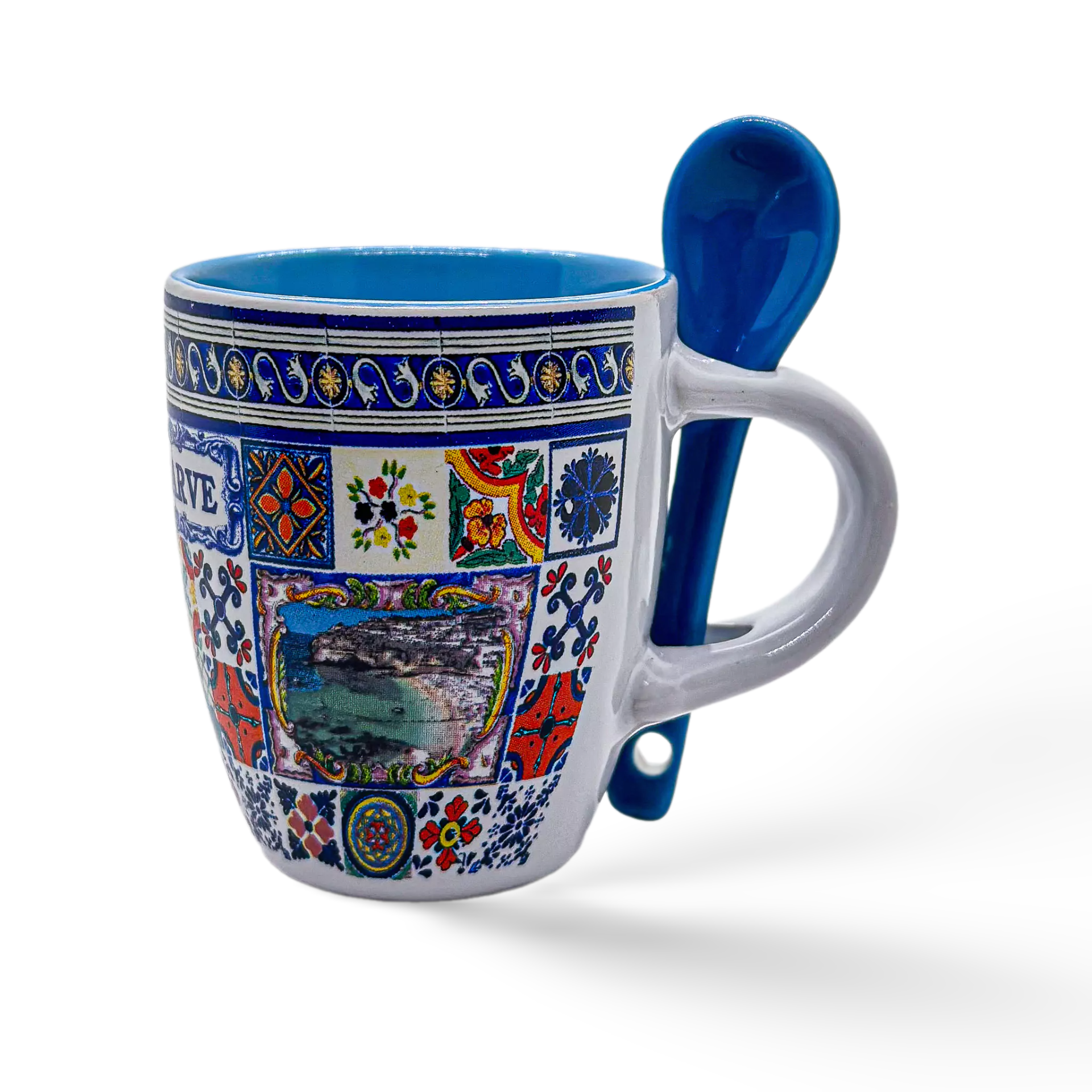 A decorative ceramic coffee cup with colorful, intricate patterns and a small scenic picture at the center. The mug has a built-in slot on the handle holding a matching blue ceramic spoon. The inside of the mug is also blue. This beautiful souvenir from Algarve stands out against its white background.