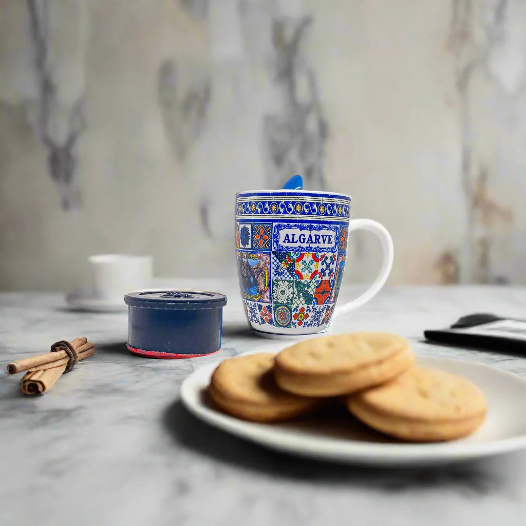 This decorative ceramic mug features detailed, colorful patterns and a scenic image at the center. It has a built-in holder on the handle for a matching blue spoon, with the inside of the cup in the same blue. A charming Algarve souvenir that contrasts beautifully with its white background.