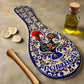 A ceramic souvenir spoon features intricate patterns in blue, yellow, and white. At its center is a vivid depiction of the famous Portuguese rooster, encircled by elegant floral designs. The word "PORTUGAL" is prominently shown at the base.