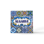 A vibrant ceramic tile magnet with "ALGARVE" boldly in the center. The tile showcases intricate blue, yellow, green, and white patterns and floral motifs, reflecting traditional Portuguese azulejos artwork. A perfect souvenir to capture the essence of Algarve.