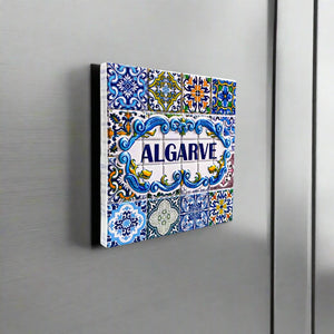 A colorful ceramic tile magnet featuring "ALGARVE" prominently in the center, surrounded by detailed blue, yellow, green, and white patterns with floral designs. Inspired by traditional Portuguese azulejos, this makes for an ideal Algarve souvenir.
