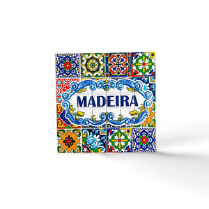 A decorative square tile, perfect as a souvenir from Portugal, showcases the word "Madeira" in blue text at its center, surrounded by intricate, colorful patterns and floral designs in shades of yellow, green, red, and blue. The white background highlights the vibrant details of this charming magnet.