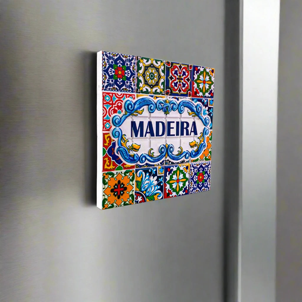 A charming square tile souvenir from Portugal featuring "Madeira" in bold blue letters at the center. Surrounding it are intricate, colorful patterns and floral designs in vibrant shades of yellow, green, red, and blue, all set against a white background that enhances the lively details of this magnet.