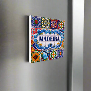A charming square tile souvenir from Portugal featuring "Madeira" in bold blue letters at the center. Surrounding it are intricate, colorful patterns and floral designs in vibrant shades of yellow, green, red, and blue, all set against a white background that enhances the lively details of this magnet.