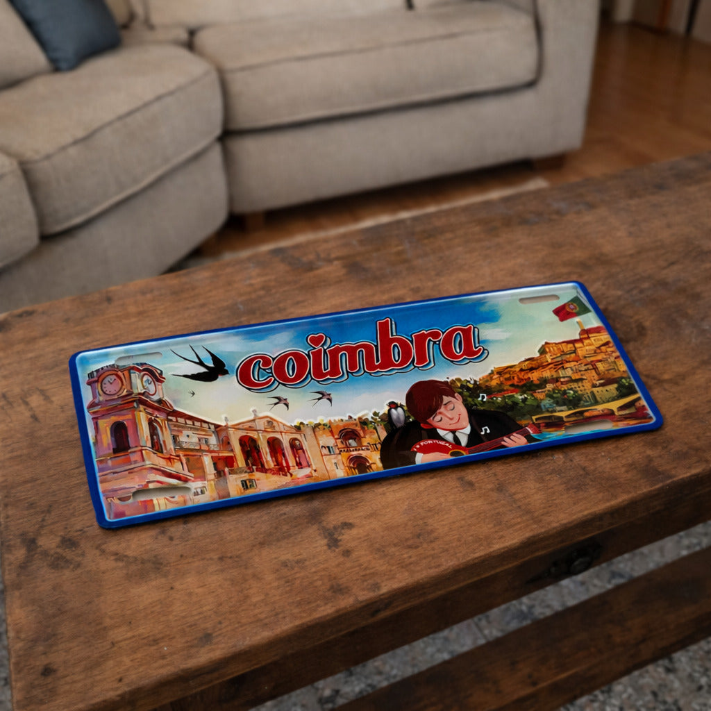 Coimbra metal souvenir sign placed on a wooden table showing university buildings, fado musician and city scenery