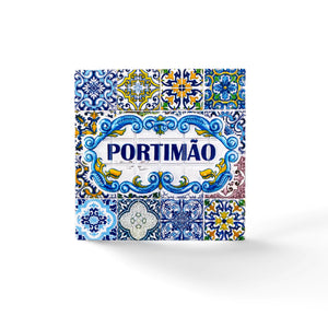 A square Portuguese ceramic tile with intricate blue, yellow, and white patterns. The center features the name "PORTIMÃO" in bold blue letters, surrounded by floral and geometric designs. The tile, reflecting the traditional Azulejo style of Portugal's Algarve region, is a beautiful piece of craftsmanship.