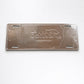 Backside of Fátima metal souvenir sign showing engraved outlines on a brushed metal surface with mounting slots
