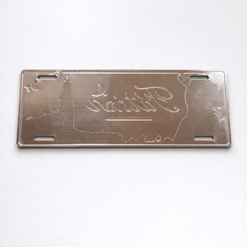 Backside of Fátima metal souvenir sign showing engraved outlines on a brushed metal surface with mounting slots