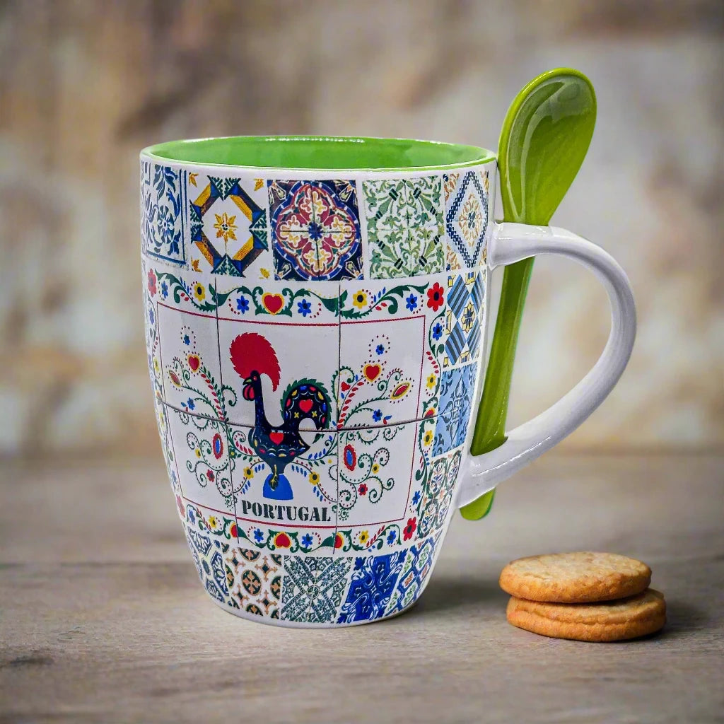 A vibrant coffee mug adorned with traditional Portuguese tile designs, showcasing the famous Barcelos Rooster at the center with the word "PORTUGAL" below. In front of this charming green Portuguese mug, a bright green spoon filled with ground coffee is placed. The background is white.