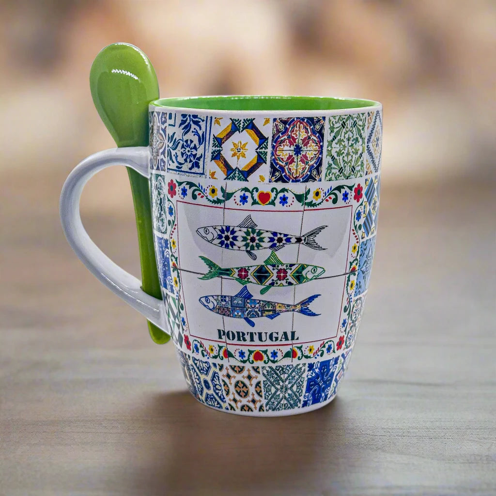 A colorful mug featuring classic Portuguese tile patterns, with the iconic Barcelos Rooster prominently displayed in the center and "PORTUGAL" written underneath. A green spoon, filled with ground coffee, is positioned in front of this attractive green Portuguese coffee mug. The image is set against a white background.