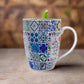 A decorative coffee mug with traditional Portuguese tile motifs, highlighting the Barcelos Rooster in the center and the word "PORTUGAL" beneath it. A bright green spoon, heaped with ground coffee, sits in front of this green Portuguese mug. The background is white.