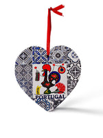 A heart-shaped ornament features a colorful rooster design with the word "Portugal" written below it. The rooster is surrounded by intricate blue and white tile patterns. A red ribbon is attached to the top for hanging, and a cork base adds a charming touch to this delightful souvenir.
