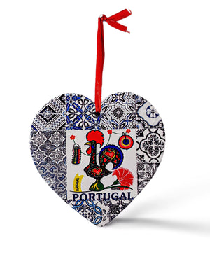 A heart-shaped ornament features a colorful rooster design with the word "Portugal" written below it. The rooster is surrounded by intricate blue and white tile patterns. A red ribbon is attached to the top for hanging, and a cork base adds a charming touch to this delightful souvenir.