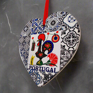 A heart-shaped ornament showcasing a vibrant rooster design with the word "Portugal" beneath it. The rooster is framed by intricate blue and white tile patterns. A red ribbon at the top allows for hanging, while a cork base adds a charming touch to this lovely souvenir.