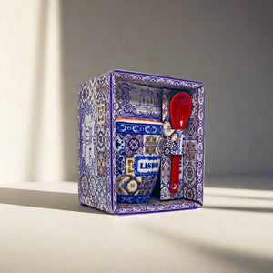 A Lisbon-themed souvenir gift set is displayed inside a decorative box with intricate blue and white patterns. The set includes a ceramic coffee cup with the word "Lisbon" on it and a red ceramic spoon. The box interior also features the same elaborate designs, making it a perfect keepsake from Portugal.