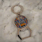 A keychain featuring a bottle opener, with a round medallion displaying a vibrant illustration of a Lisbon tram and the word "Lisboa" at the top. The background showcases a pattern inspired by traditional Portuguese tiles, making this a delightful souvenir.