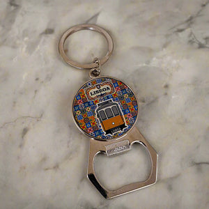 A keychain featuring a bottle opener, with a round medallion displaying a vibrant illustration of a Lisbon tram and the word "Lisboa" at the top. The background showcases a pattern inspired by traditional Portuguese tiles, making this a delightful souvenir.