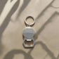 A keychain combined with a bottle opener, highlighted by a circular element depicting a colorful Lisbon tram and the word "Lisboa" above it. The backdrop is adorned with a design reminiscent of classic Portuguese tiles, adding to the charm of this souvenir.