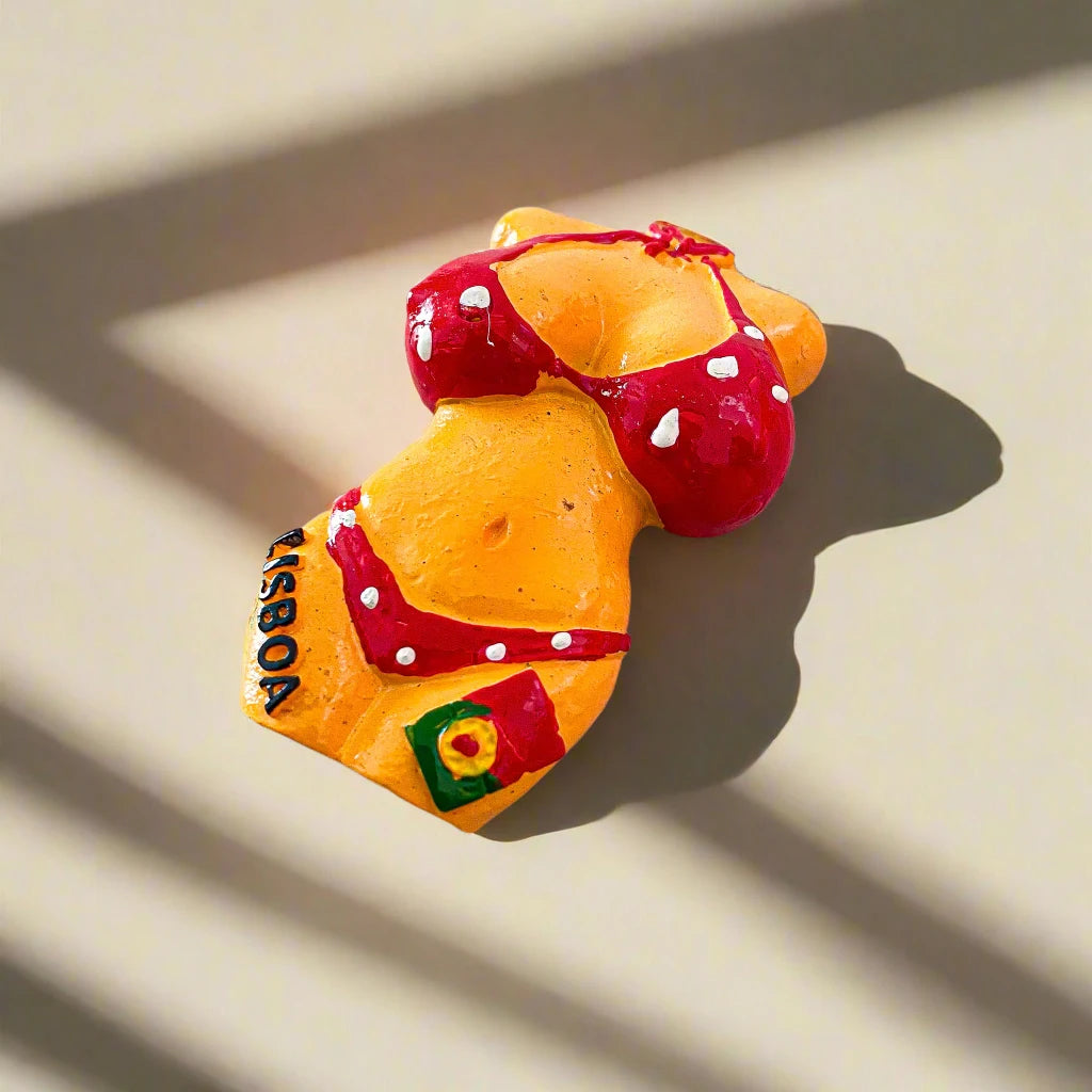 A vibrant magnet featuring a torso figurine dressed in a red polka dot bikini. The bikini bottoms display the word "Lisboa" along with a small flag emblem, celebrating Lisbon. The figurine pops against a simple white background.