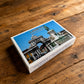 Lisbon souvenir playing cards box displayed on a rustic wooden table, featuring Praça do Comércio with Rua Augusta Arch and the King José I statue.