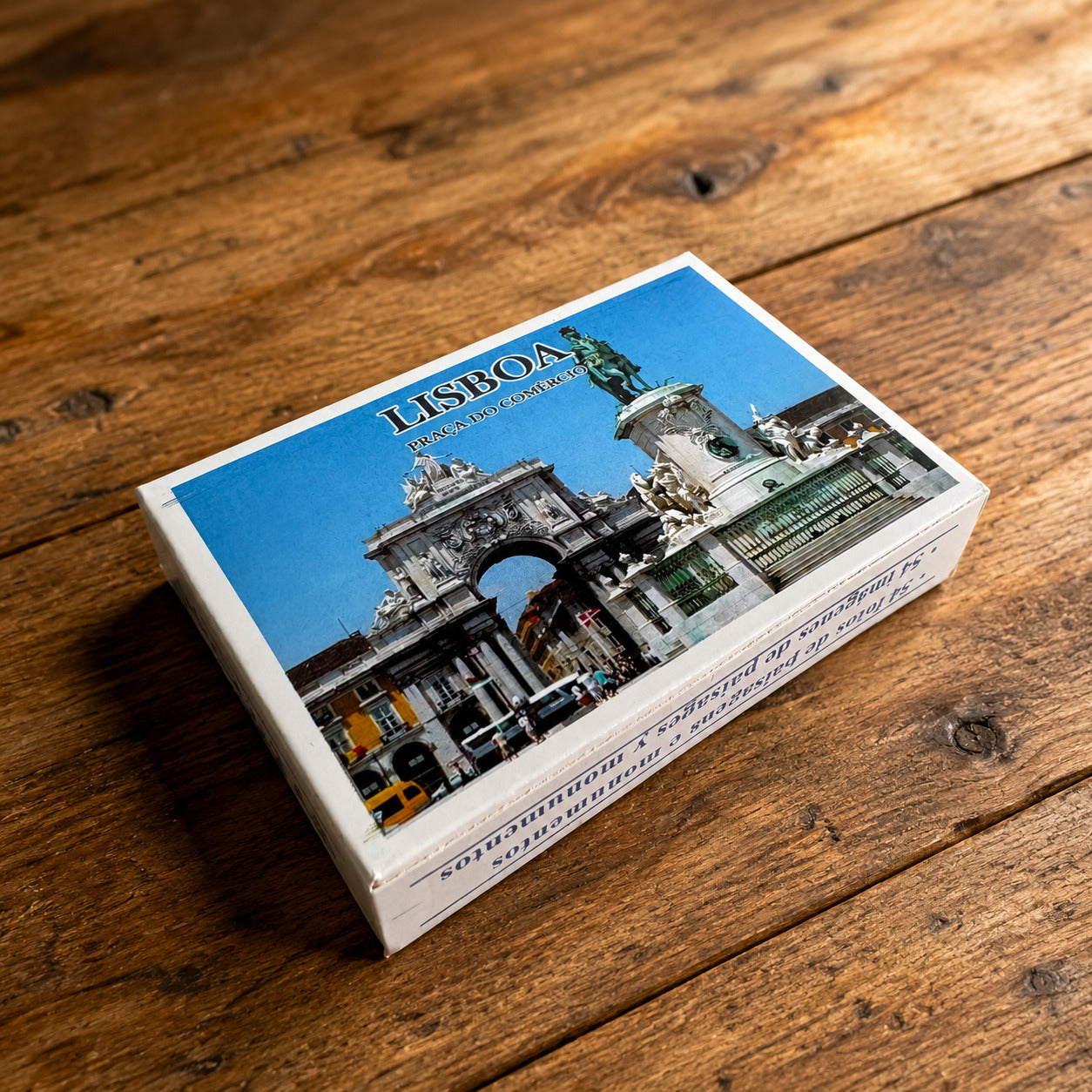 Lisbon souvenir playing cards box displayed on a rustic wooden table, featuring Praça do Comércio with Rua Augusta Arch and the King José I statue.