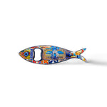 A metal fish-shaped bottle opener, designed to represent a sardine, is adorned with colorful, intricate details including a landmark building and the text "Lisboa." This charming Portugal souvenir features an opener hole where the fish's eye would be.