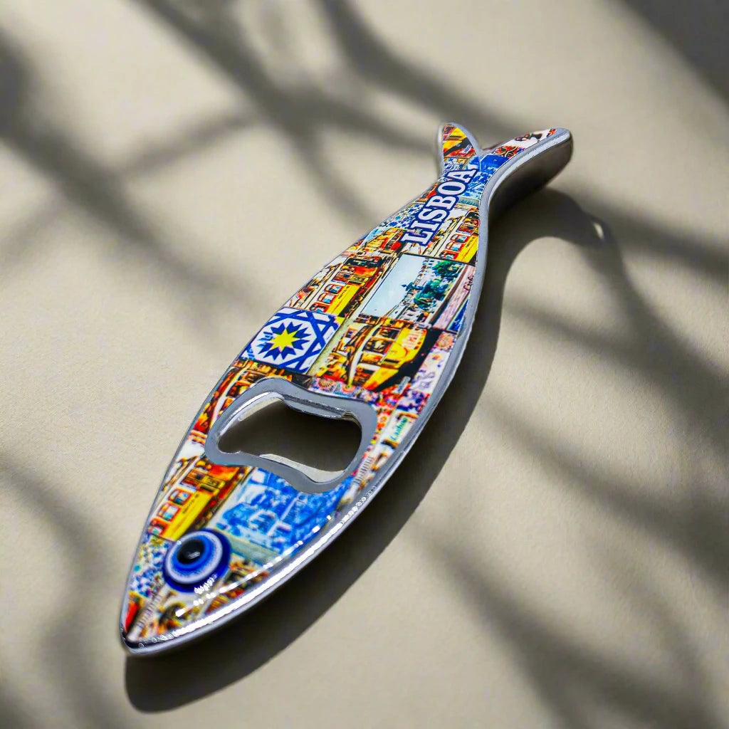 A metal bottle opener in the shape of a sardine, featuring detailed and colorful designs, including a notable Lisbon landmark and the word "Lisboa." The opener hole is creatively placed at the fish's eye, making it a unique souvenir from Portugal.