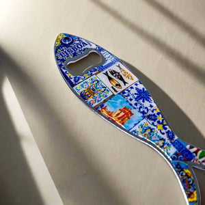 A sardine-inspired metal bottle opener, decorated with colorful and detailed artwork that includes a Lisbon landmark and the word "Lisboa." The opener hole is placed at the fish's eye, making it a delightful Portuguese souvenir.