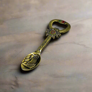 A unique souvenir from Lisbon, Portugal, combining a decorative magnet, bottle opener, and spoon. The handle showcases the Portuguese coat of arms with "Lisboa" engraved along the stem, while the spoon features a traditional scene, reflecting cultural or historical significance.