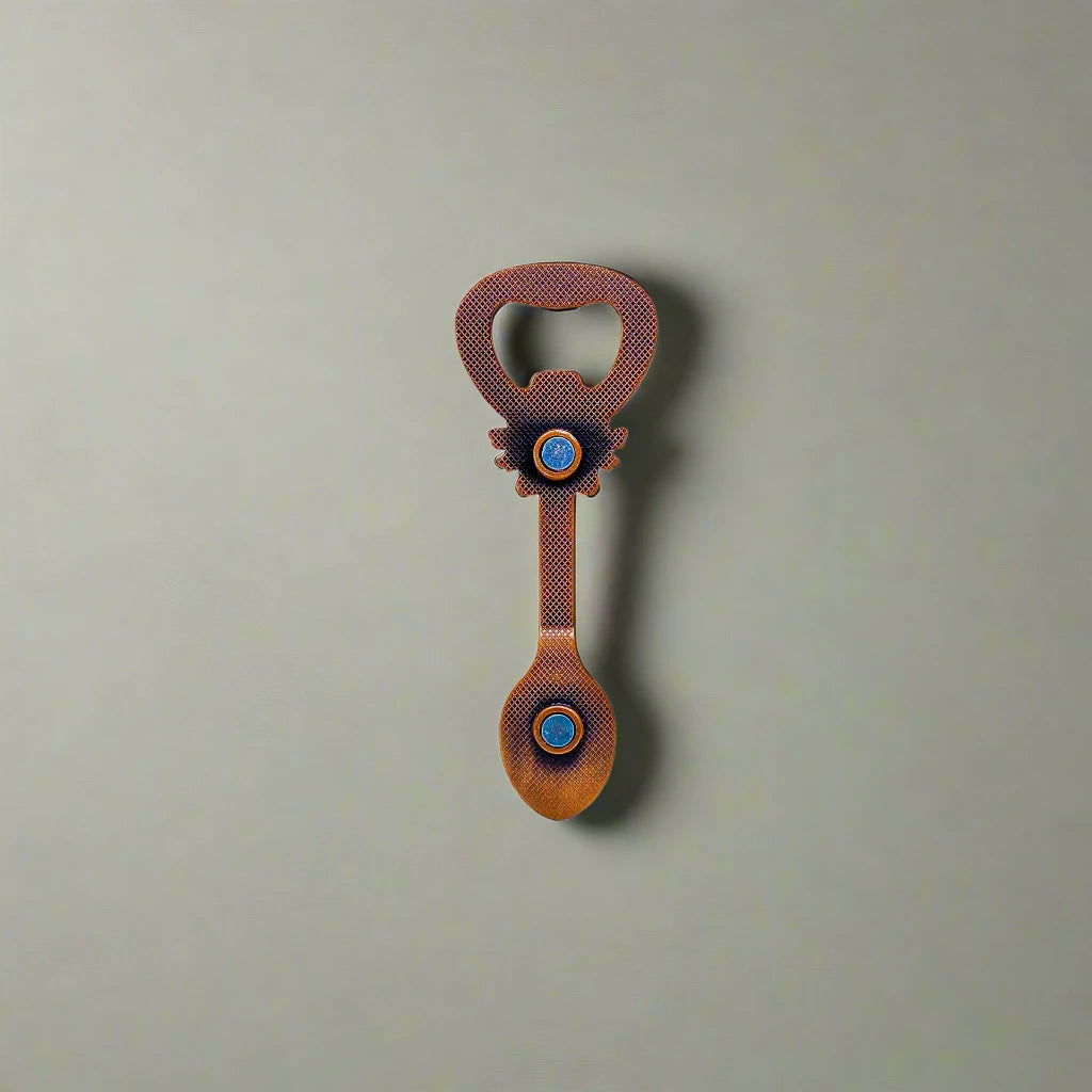 This elegant bottle opener, designed in the shape of a spoon, features "LISBOA" along with ornate patterns, a crested emblem, and a detailed scene within the spoon. The handle displays the flag of Portugal, and a magnet on the back makes it perfect for displaying on your fridge. 