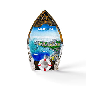 Souvenir magnet shaped like a boat with "MADEIRA" at the top. This charming keepsake features a scenic view of Madeira with blue waters, boats, cliffside houses, and a lifebuoy at the bottom. Perfect for any magnet collection or as a nostalgic reminder of your trip to this beautiful island.