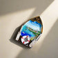 A boat-shaped souvenir magnet with "MADEIRA" displayed at the top. This delightful keepsake captures a picturesque view of Madeira, featuring blue waters, boats, cliffside homes, and a lifebuoy at the bottom. Ideal for a magnet collection or as a cherished memento of your visit to this stunning island.