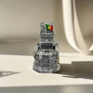A detailed miniature replica of Lisbon's iconic Belem Tower is displayed, with the word "PORTUGAL" elegantly inscribed in gold at the base. The intricate design of the tower stands out against a clean, white background.