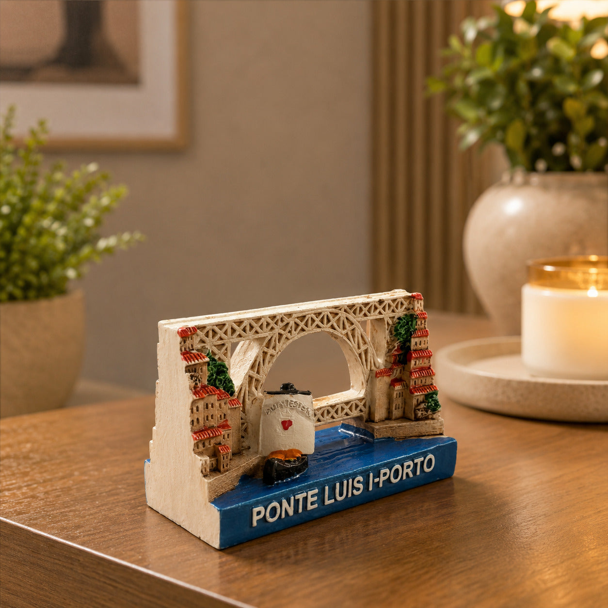 Porto Dom Luís I Bridge souvenir magnet displayed on a wooden table, featuring the iconic iron bridge crossing the Douro River with traditional Ribeira houses and a Port wine boat.