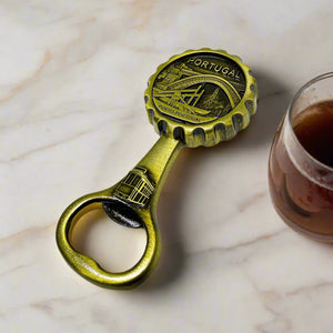 A decorative brass bottle opener with an engraved Porto, Portugal design. The round top depicts a detailed scene of the Dom Luís I Bridge, a classic tram, and city views, along with the inscriptions "PORTUGAL" and "PORTO-PORTUGAL."