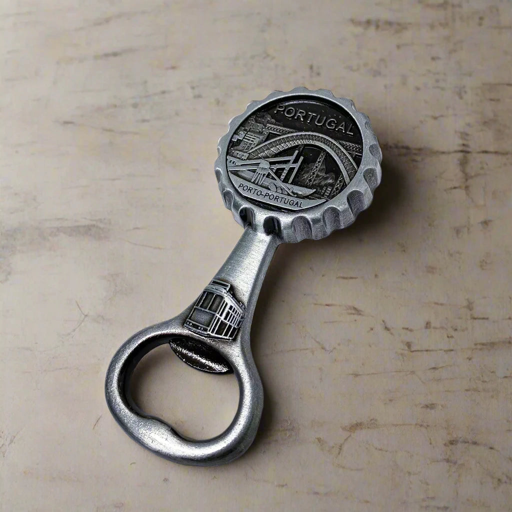 A decorative brass bottle opener with an engraved Porto, Portugal design. The round top depicts a detailed scene of the Dom Luís I Bridge, a classic tram, and city views, along with the inscriptions "PORTUGAL" and "PORTO-PORTUGAL."