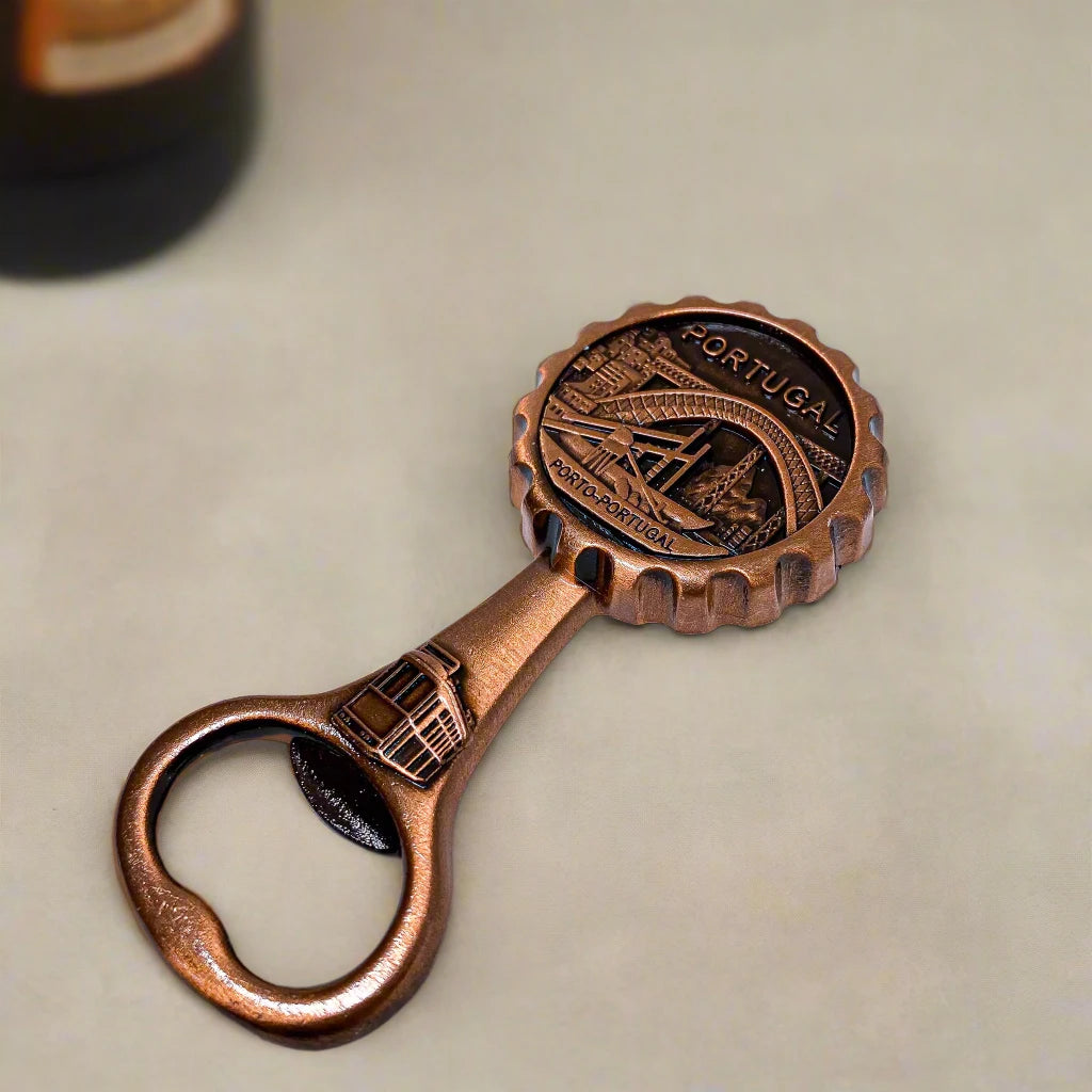 A decorative brass bottle opener featuring an engraved depiction of Porto, Portugal. The round top includes intricate illustrations of the Dom Luís I Bridge, a traditional tram, and city landmarks, with the words "PORTUGAL" and "PORTO-PORTUGAL" inscribed.