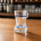 Side profile of Porto souvenir shot glass with transparent glass body, blue stripe decoration, and traditional Portuguese azulejo inspired bikini artwork.