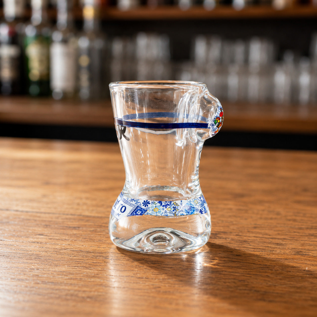 Side profile of Porto souvenir shot glass with transparent glass body, blue stripe decoration, and traditional Portuguese azulejo inspired bikini artwork.