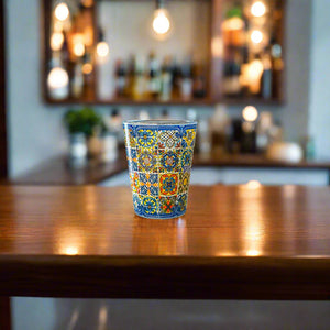 Portugal souvenir shot glass featuring intricate blue and yellow Portuguese tile designs placed on a wooden surface in a bar setting.
