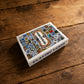 Portugal souvenir playing cards box displayed on a rustic wooden table, featuring an azulejo-inspired cover design with Portuguese landmarks, symbols, and decorative tiles.