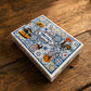 Portugal souvenir playing cards box displayed on a rustic wooden surface, decorated with traditional azulejo motifs, yellow tram, Barcelos rooster, Portuguese guitar, and cultural illustrations.