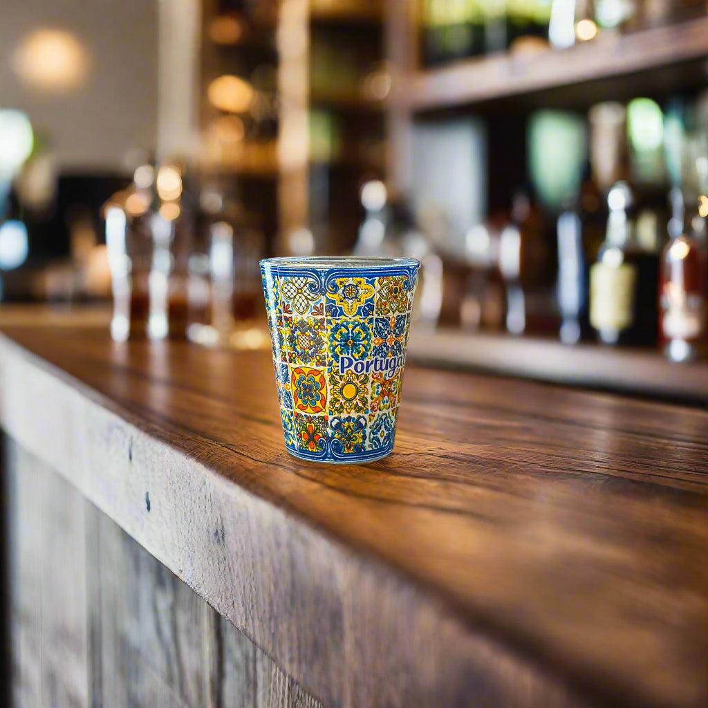 Portugal souvenir shot glass decorated with vibrant traditional azulejo tile artwork displayed on a rustic wooden bar counter.