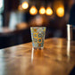 Portugal souvenir shot glass decorated with colorful traditional Portuguese azulejo tile artwork displayed on a wooden bar counter.