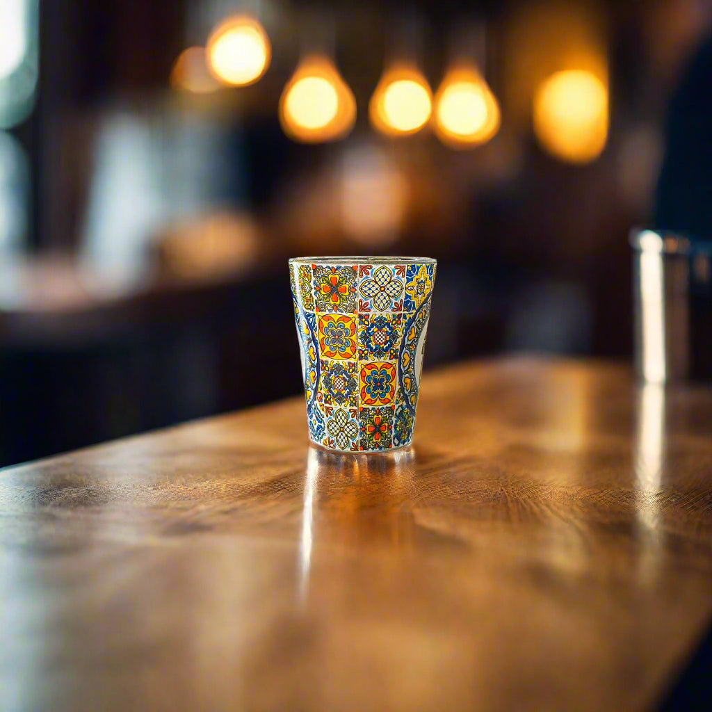 Portugal souvenir shot glass decorated with colorful traditional Portuguese azulejo tile artwork displayed on a wooden bar counter.
