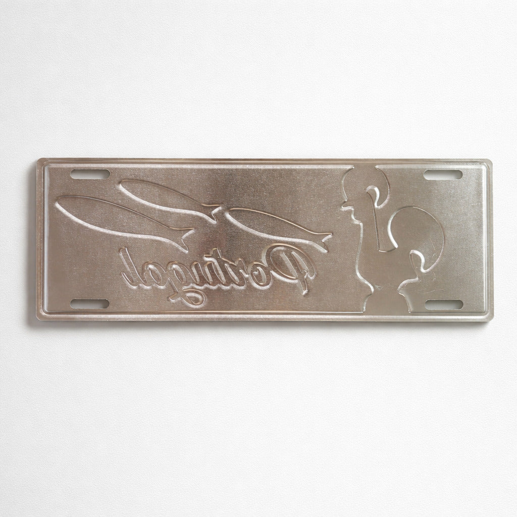 Backside of Portugal metal souvenir sign showing engraved rooster and sardine shapes on a metallic surface